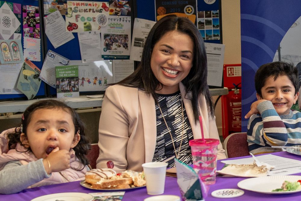 children and adult smiling and eating together at a community lunch