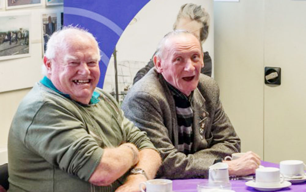 two adults together in a community space having a cup of tea and laughing