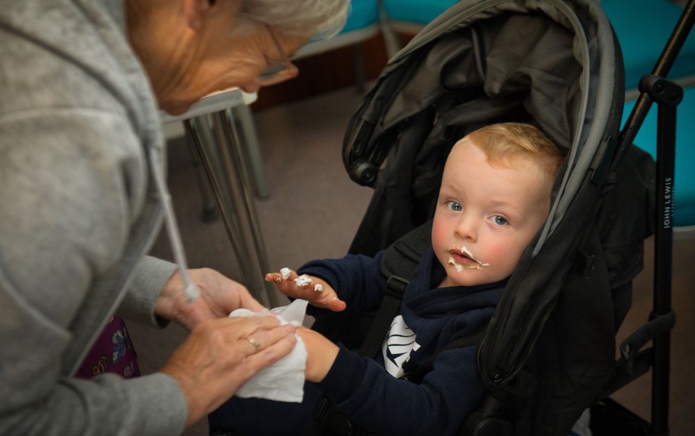 a child eating food whilst having their hands cleaned by an adult