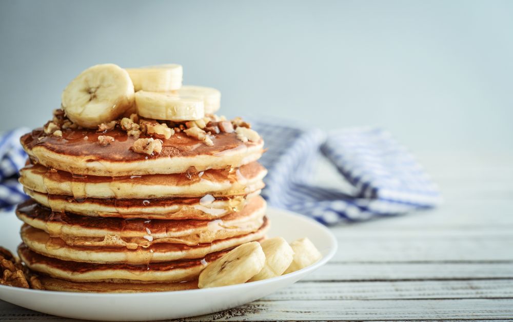 stack of pancakes with bananas and maple syrup